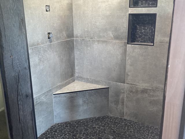 Grey tile shower with pebble floor and corner seat